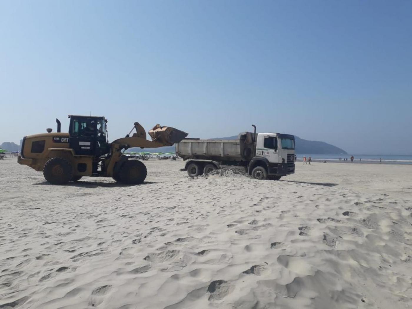 retroescavadeira leva areia para outro caminhão na praia #paratodosverem