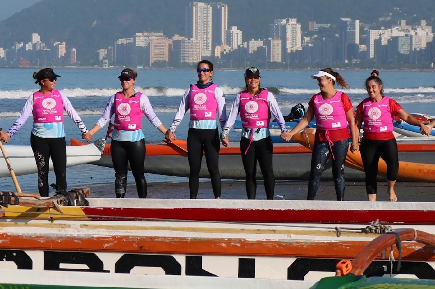 mulheres com colete ao lado de canoa na praia #paratodosverem