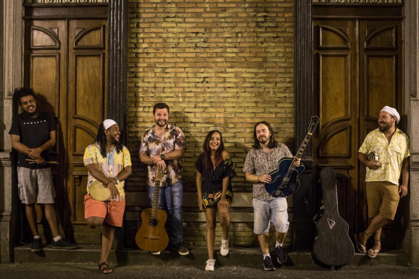 pessoas encostadas em uma parede, algumas com instrumentos musicais #paratodosverem