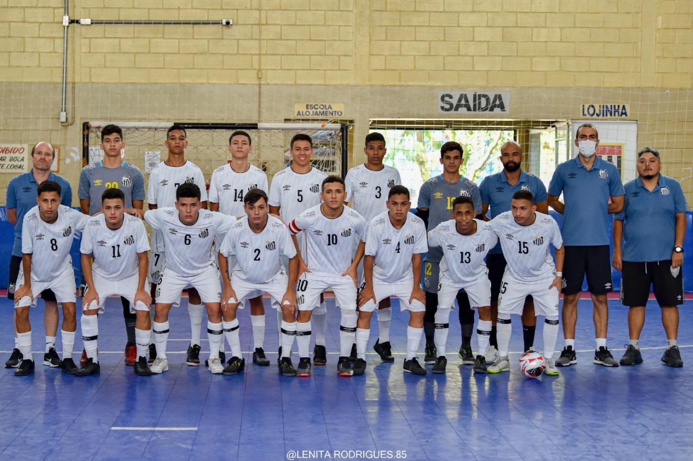 atletas usando uniforme branco , em duas fileiras, abraçados , em uma quadra #paratodosverem