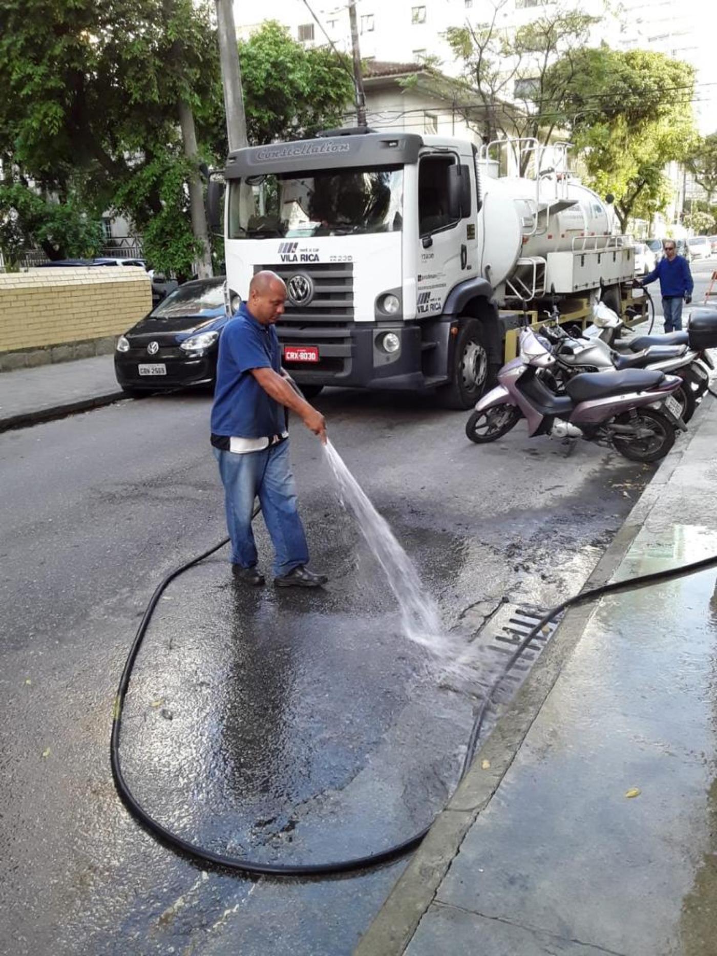 homem segura mangueira que joga água em rua #paratodosverem