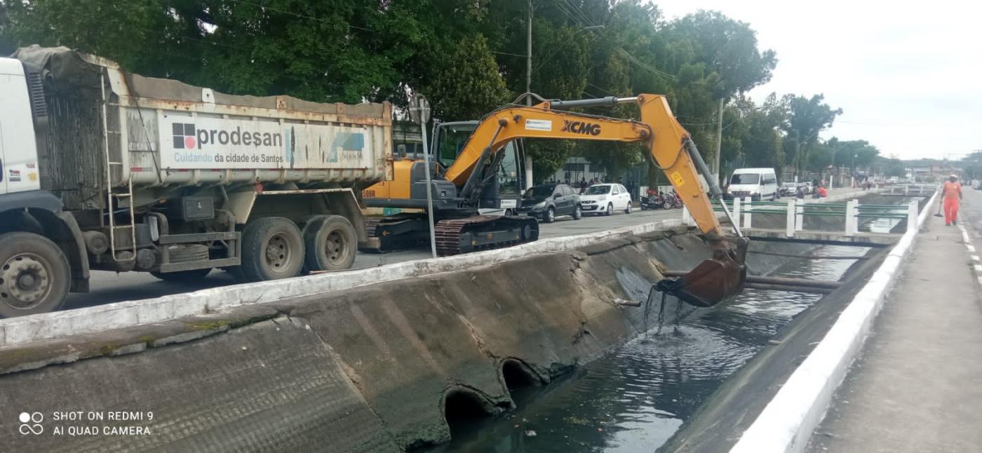 retroescavadeira ao lado de caminhão retira lama de canal #paratodosverem