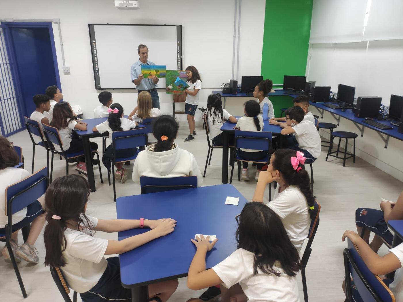 pai de aluno lê livro e crianças observam em sala de aula #paratodosverem