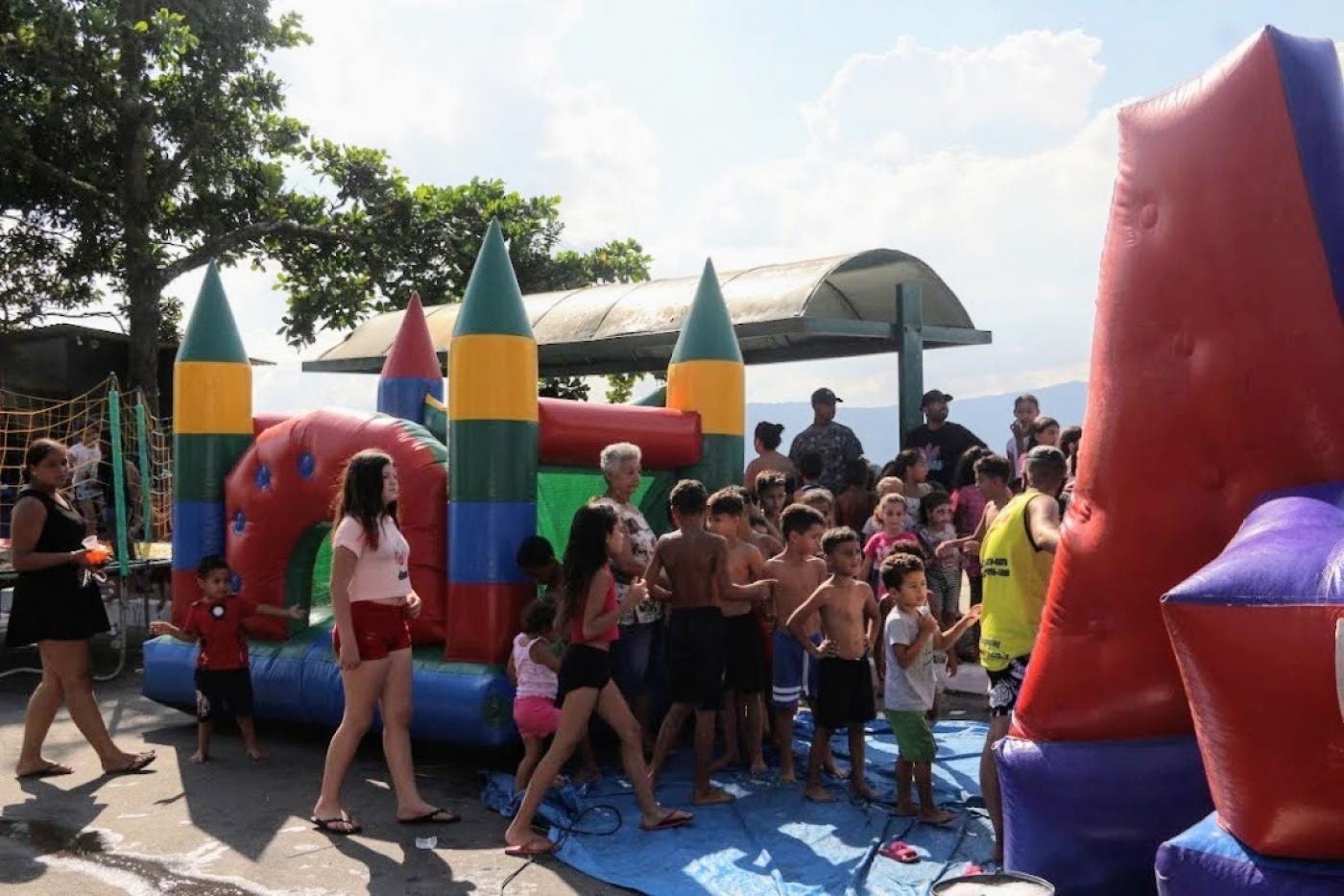 crianças em fila perto de um brinquedo colorido #paratodosverem