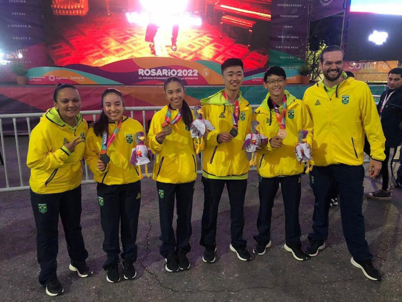 atletas com casaco amarelo mostram medalhas #paratodosverem