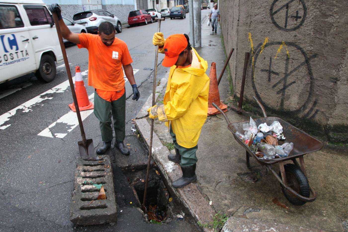 duas pessoas perto de um bueiro com equipamento de limpeza #paratodosverem