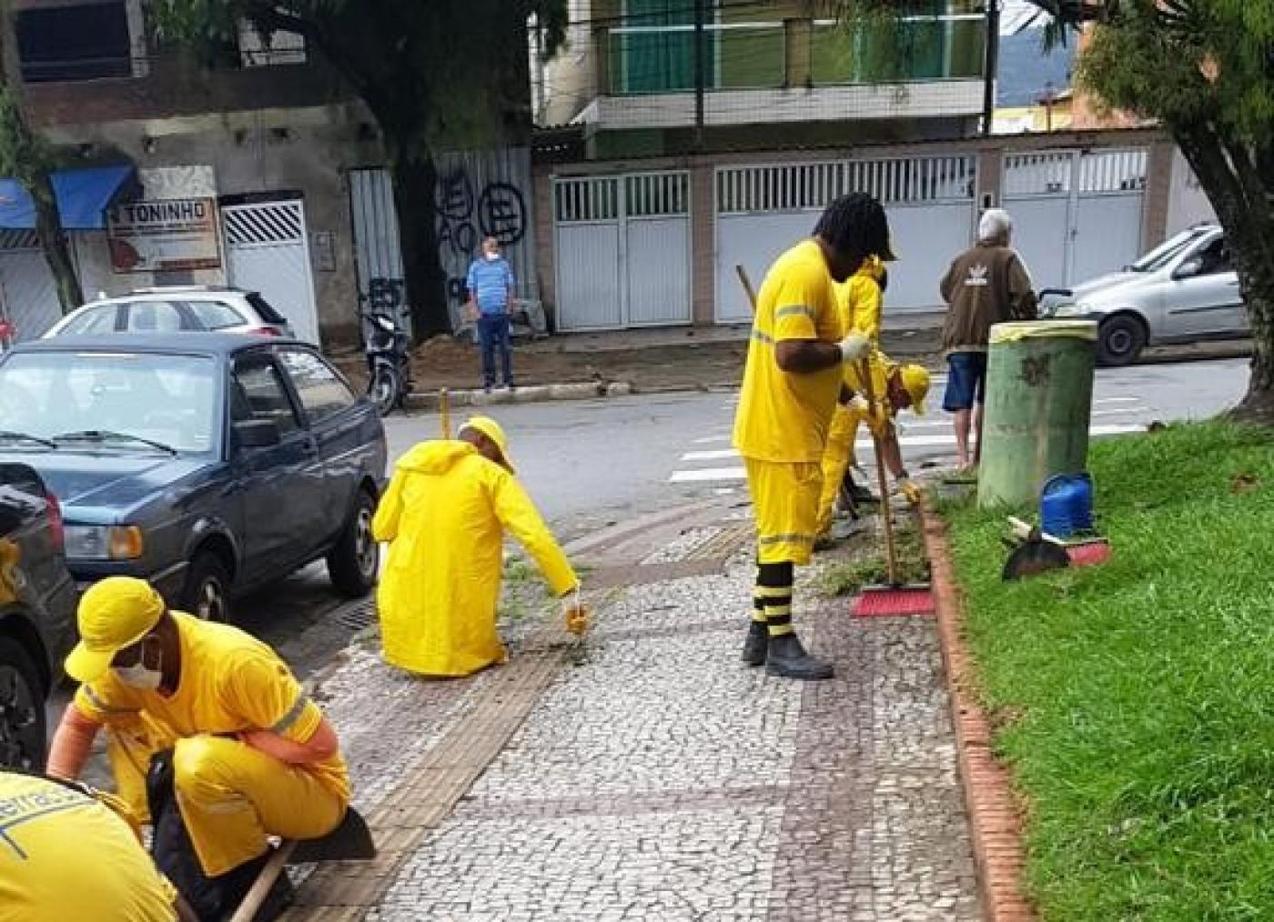 trabalhadores realizam serviços de raspação agachados no meio fio e ao lado de jardim #paratodosverem