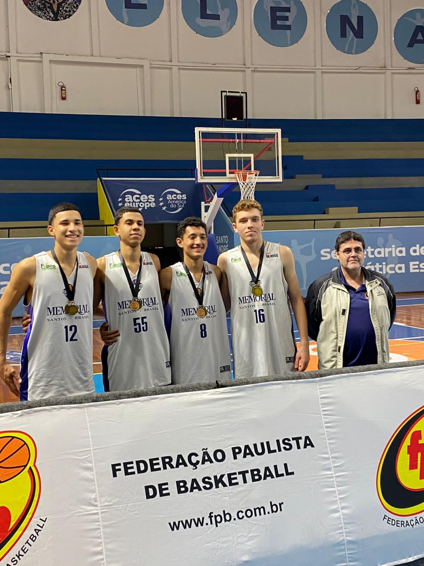 atletas no ginásio com medalhas atrás de banner #paratodosverem