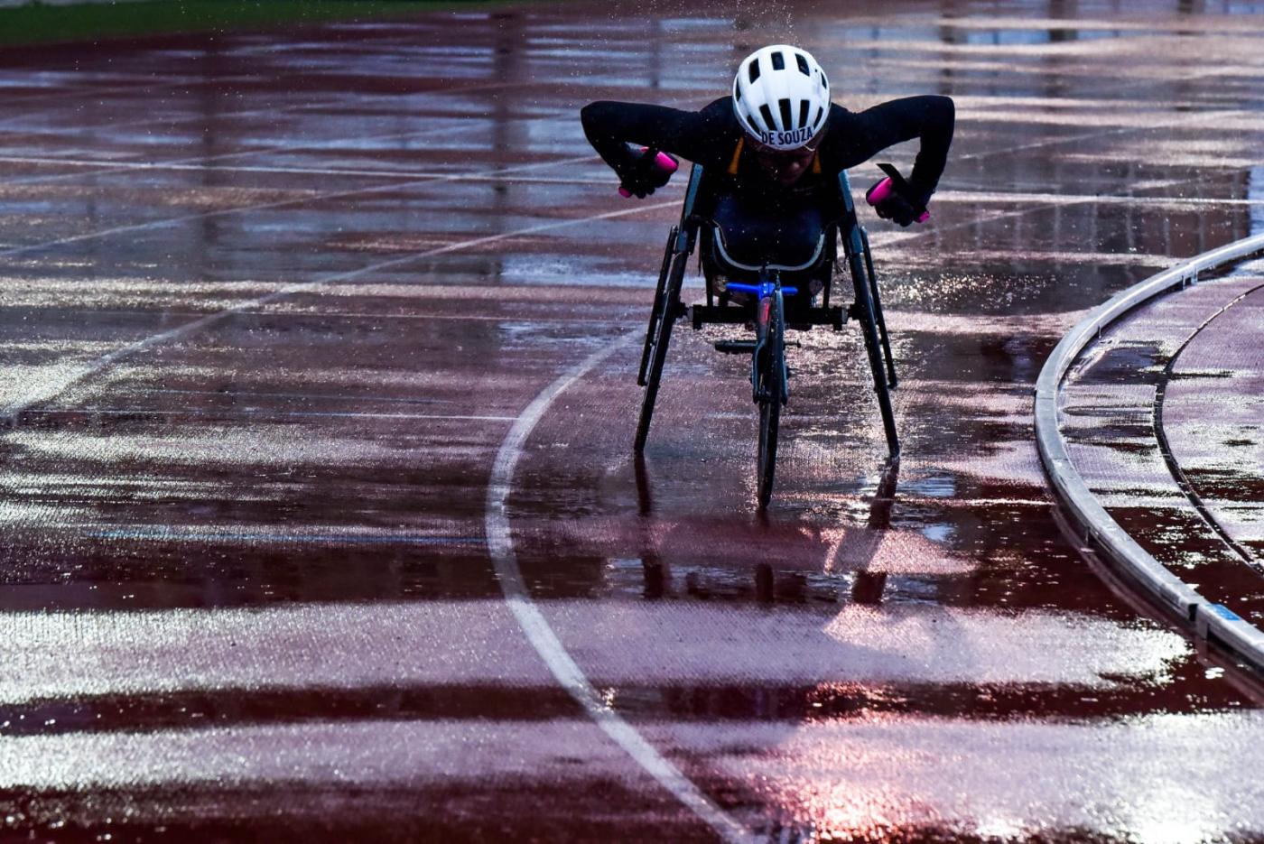 atleta na cadeira de rodas correndo um pista de atletismo molhada #paratodosverem