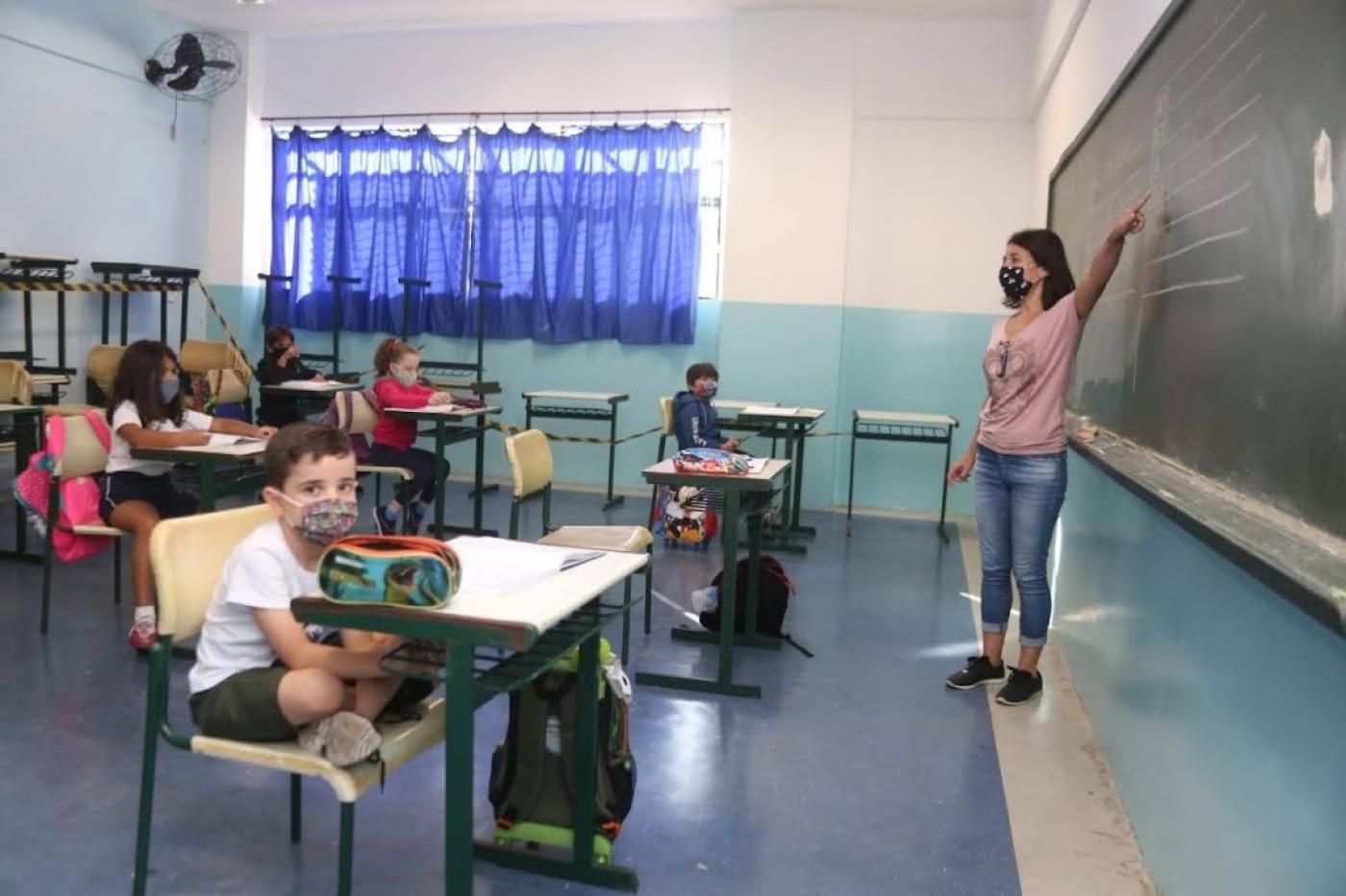 professora dá aula e crianças sentadas na sala #paratodosverem