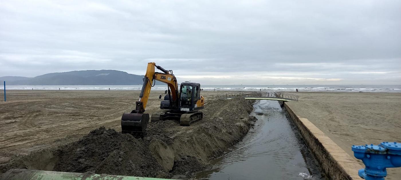 retroescavadeira retira areia ao lado de canal na praia #paratodosverem