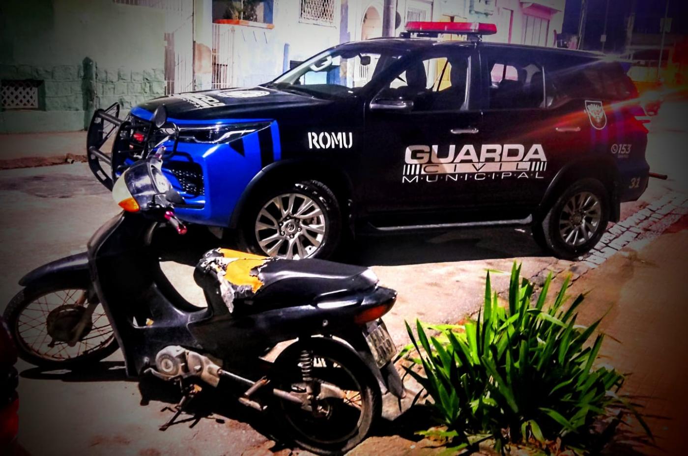 uma motocicleta em primeiro plano e a viatura da guarda municipal ao fundo. #paratodosverem 