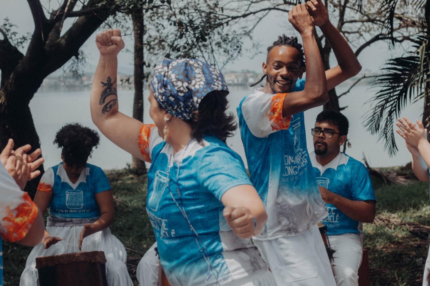 roda de dança com foco em casal que se movimenta no centro com os braços para cima. #paratodosverem 