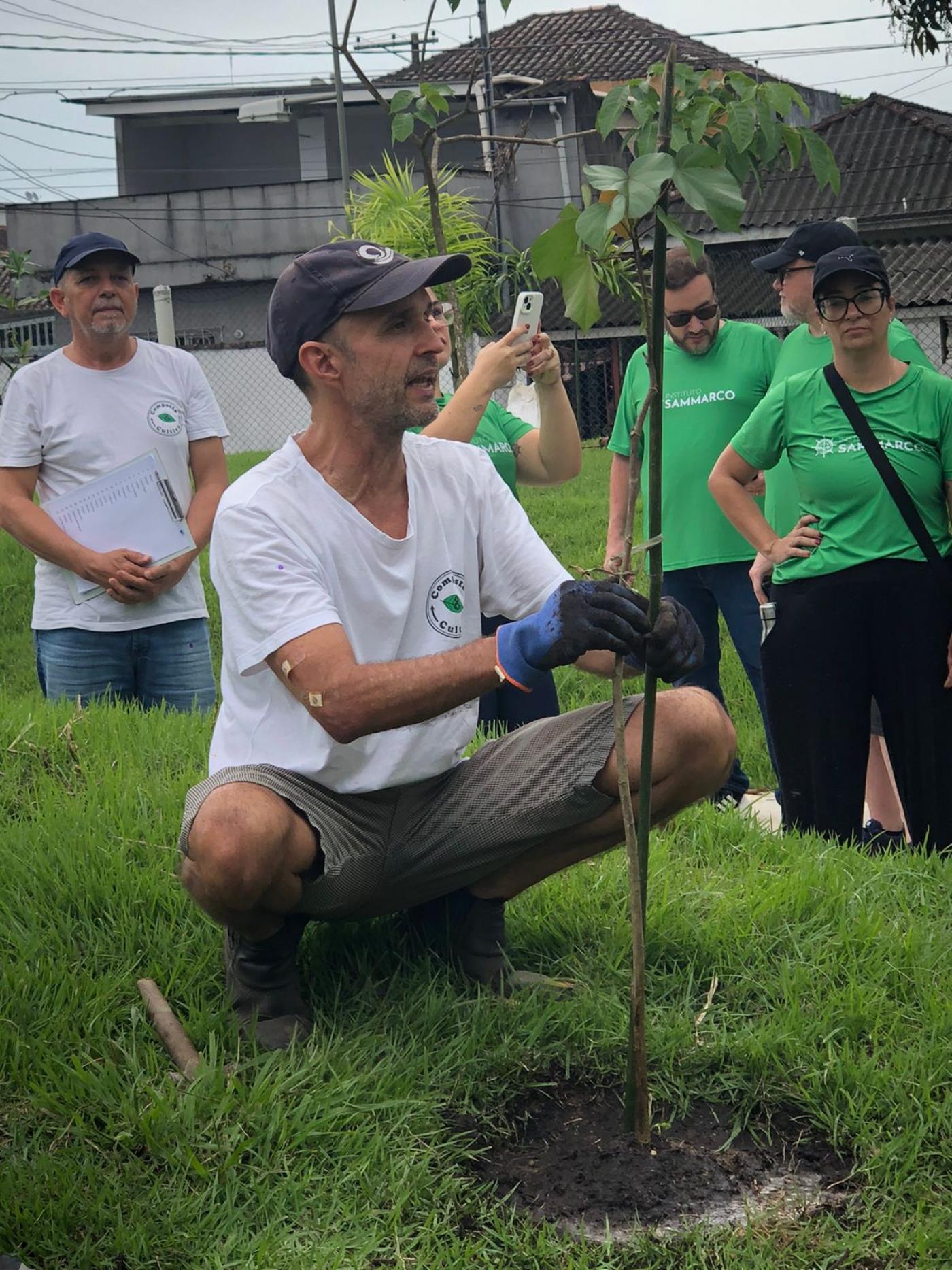 homem planta muda de árvore sobre gramado. #paratodosverem 