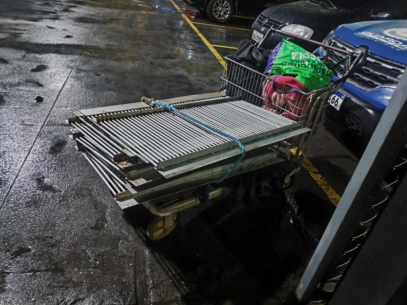 carrinho de supermercado com grelhas de ferro. A viatura da guarda municipal está atrás. #paratodosverem 