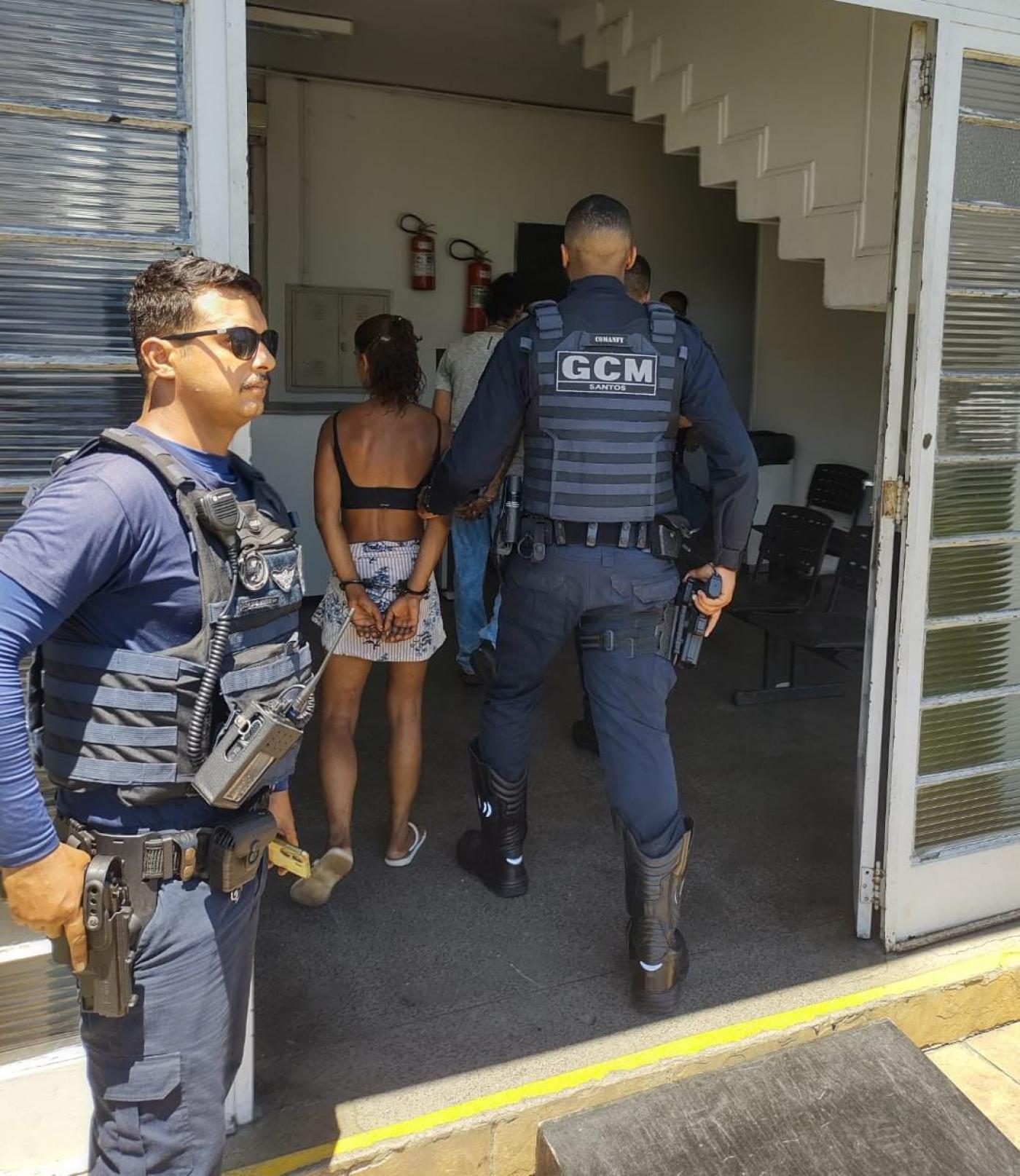 guarda municipal parado na porta de distrito policial e outro dentro do recinto, conduzindo uma mulher. #paratodosverem 
