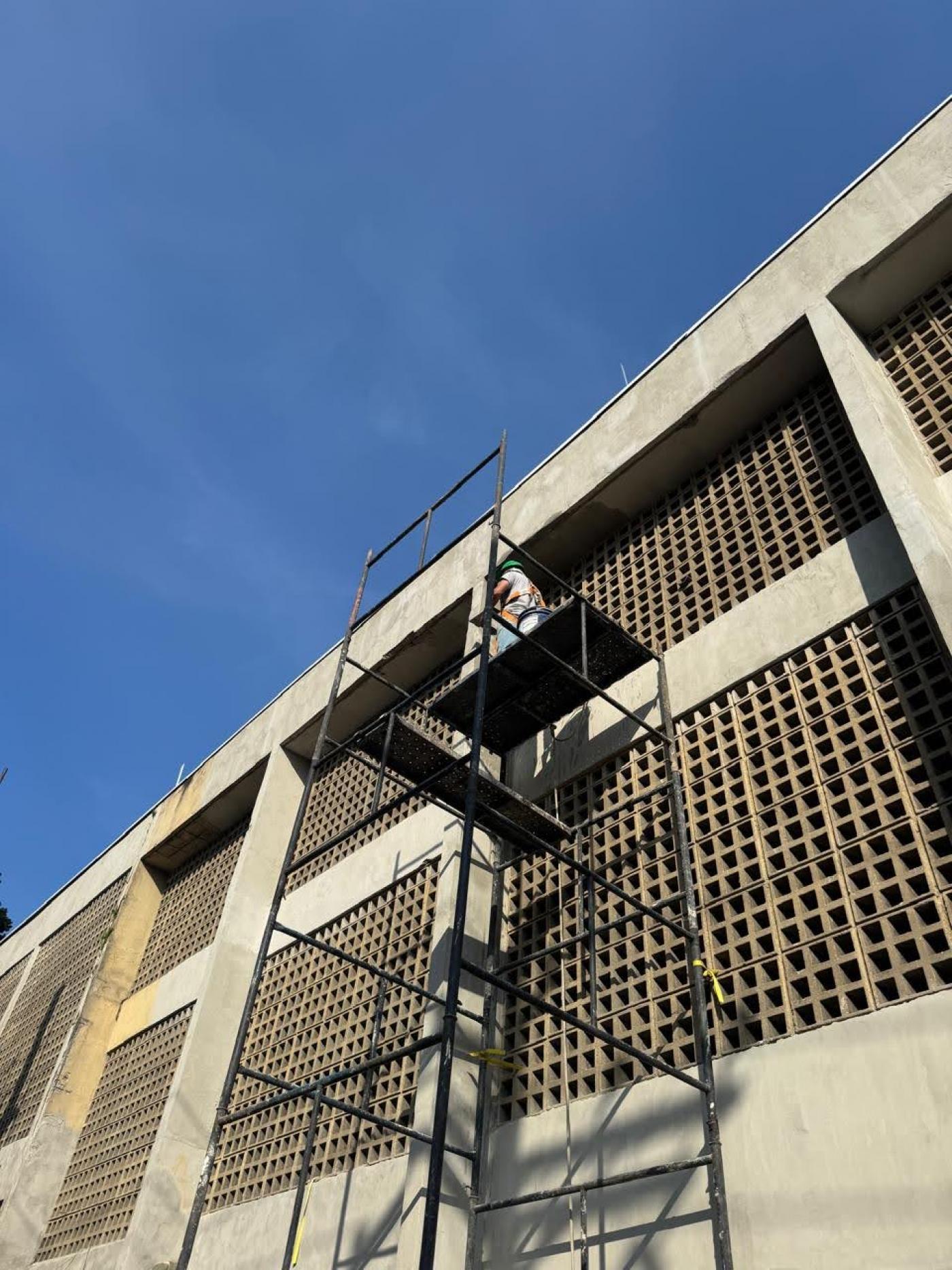 homem está em andaime trabalhando em fachada de prédio. #paratodosverem
