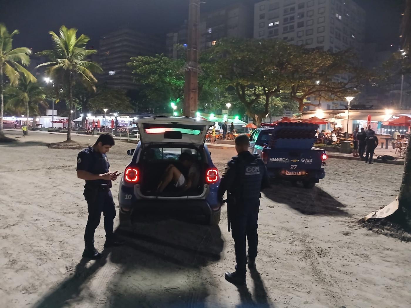 jovem dentro de viatura da guarda com dois agentes fora. #paratodosverem
