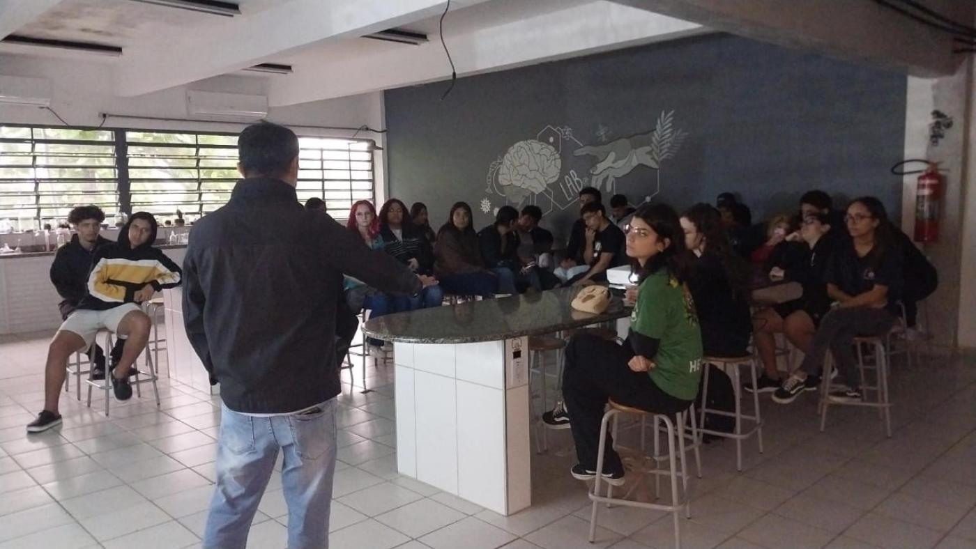 homem de costas fala a estudantes em sala de aula. #paratodosverem