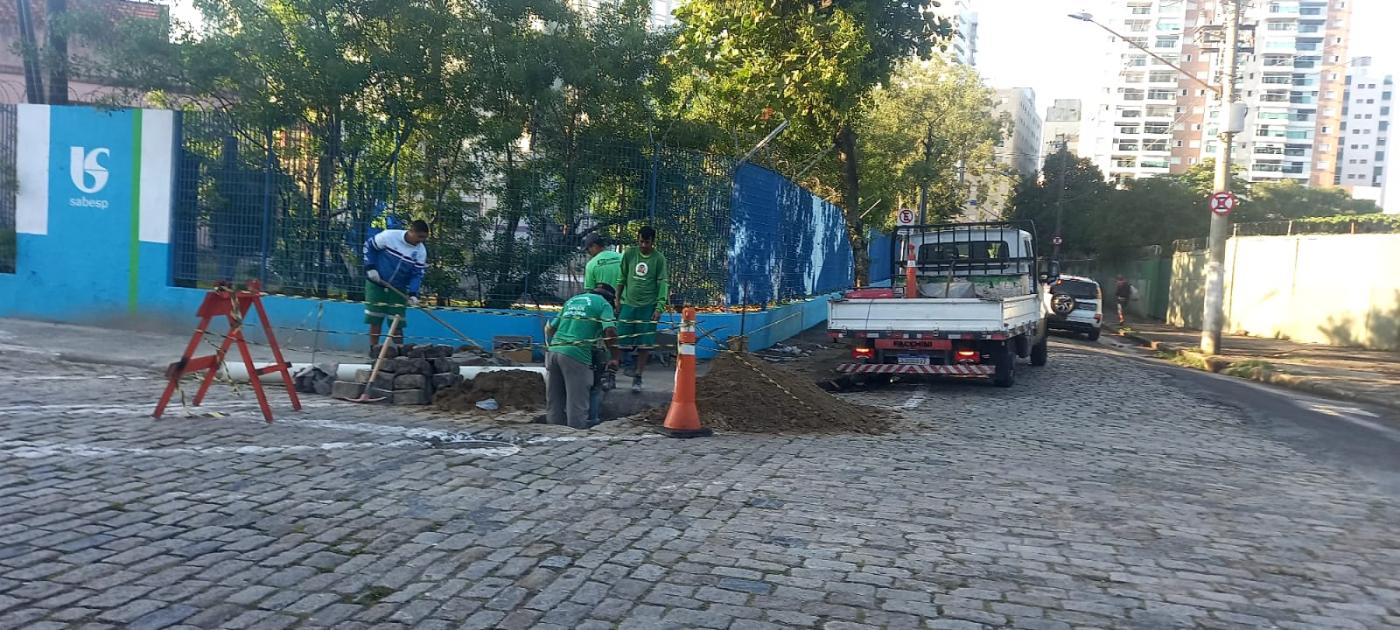 homens estão trabalhando em rede de drenagem. Paralelepípedos estão soltos para permitir acesso à rede. #paratodosverem 