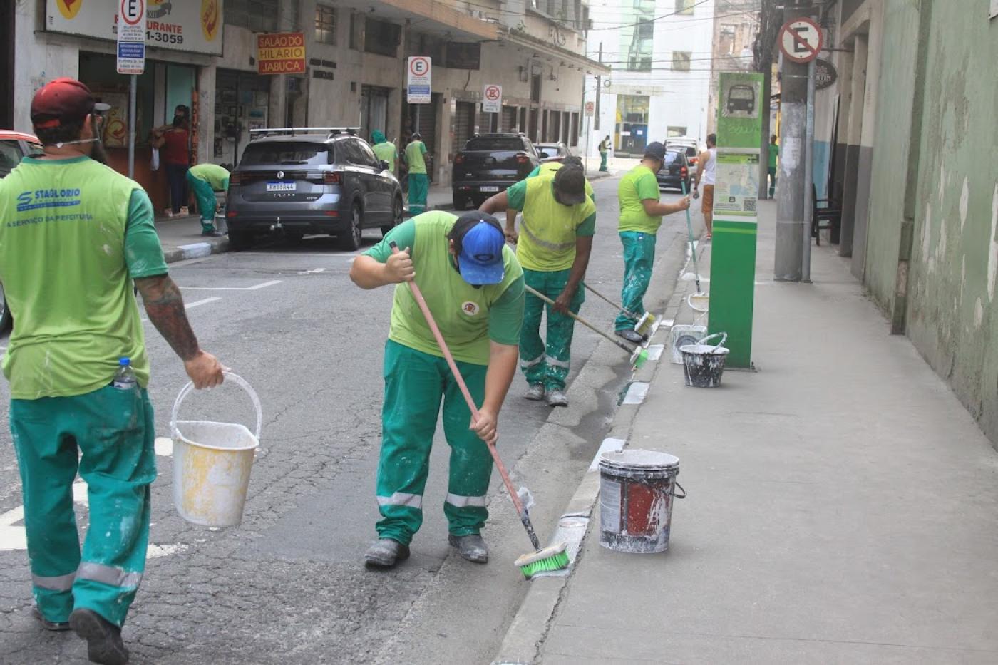Homens realizam pintura das guias na calçada #paratodosverem