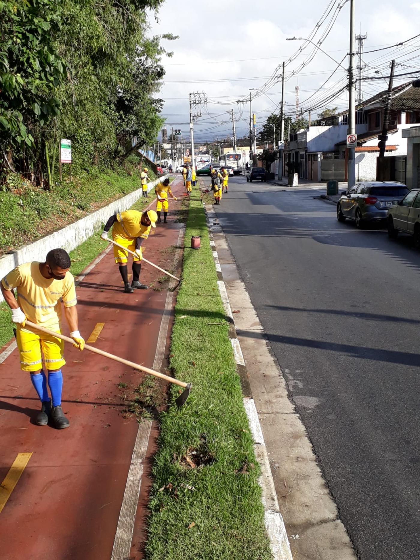 Trabalhando realizam serviço de capinação em canteiro ao lado de ciclovia. #paratodosverem