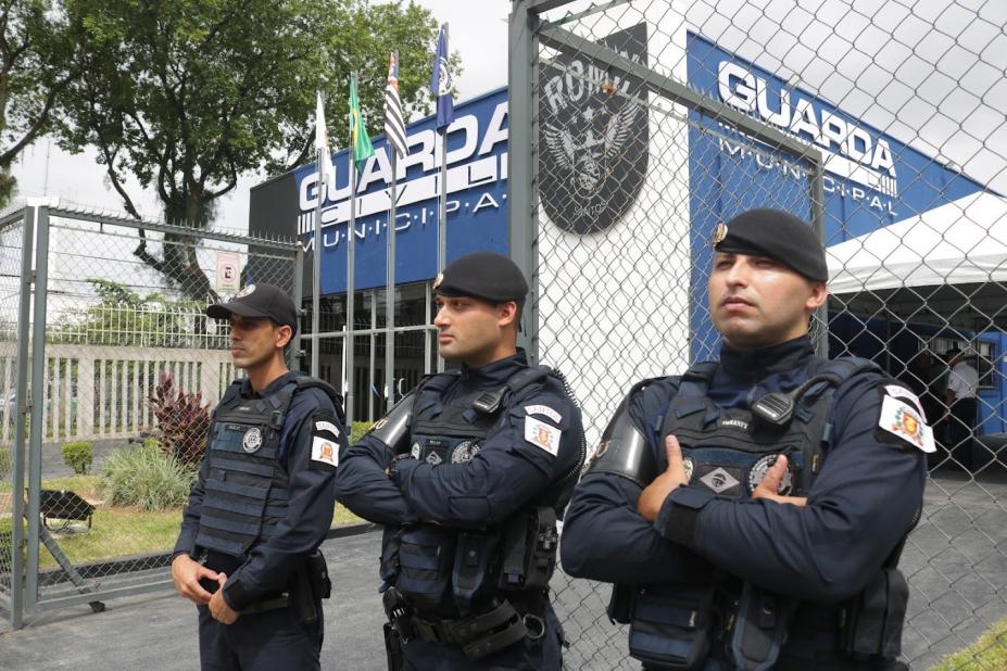 três guardas municipais parados diante de prédio da corporação onde se lê guarda municipal na fachada. #paratodosverem 