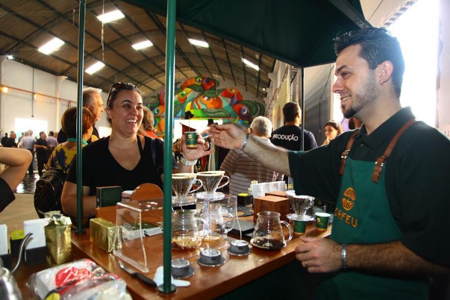 homem usando avental está preparando e servindo cafezinhos. #paratodosverem 