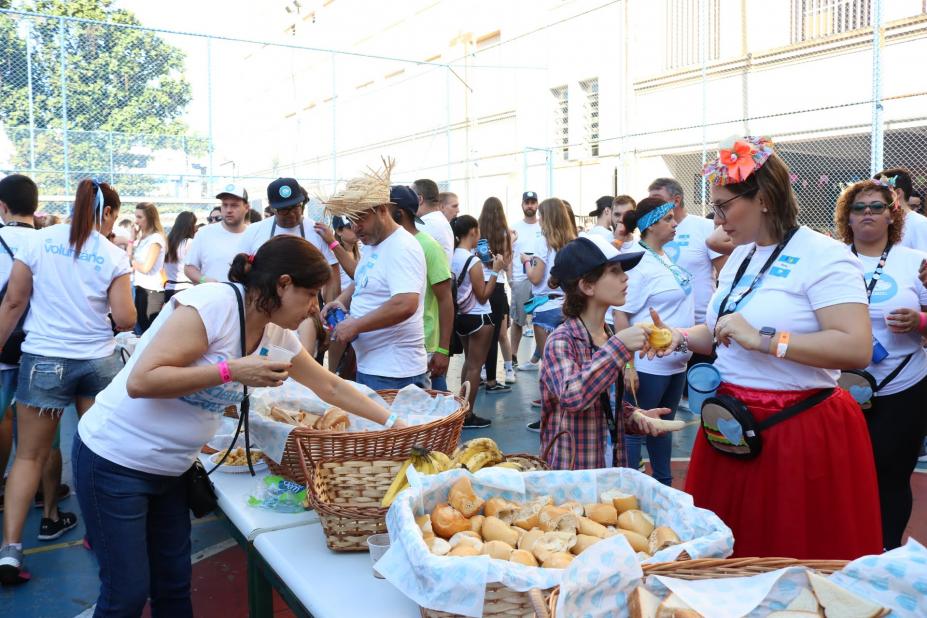 No pátio da escola, mesa posta com pães é rodeada por voluntários do projeto uniformamizados de camiseta branca