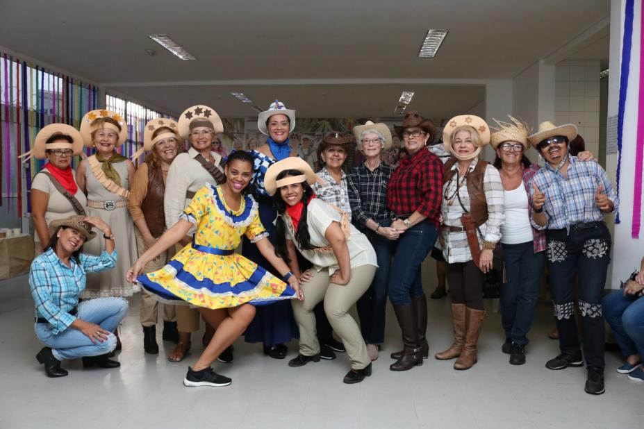 Quatorze mulheres com trajes de festa junino, femininos e masculinos, posam para foto