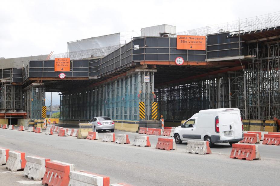 Grande estrutura em ferro que sustenta a obra de viaduto. Carros passam pista abaixo da obra. #Paratodosverem