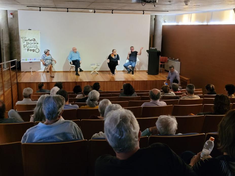 publico está sentado em auditório assistindo palestra. #paratodosverem