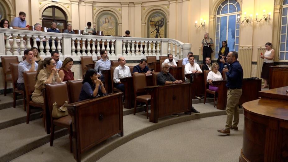 sala princesa isabel com secretários sentados e um deles em pé falando ao grupo. #paratodosverem 