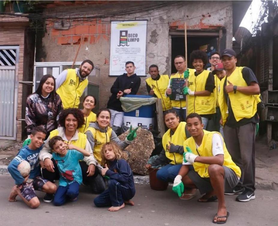 jovens uniformizados e reunidos para foto. Na casa ao fundo está afixada uma placa onde se lê Beco Limpo. #paratodosverem