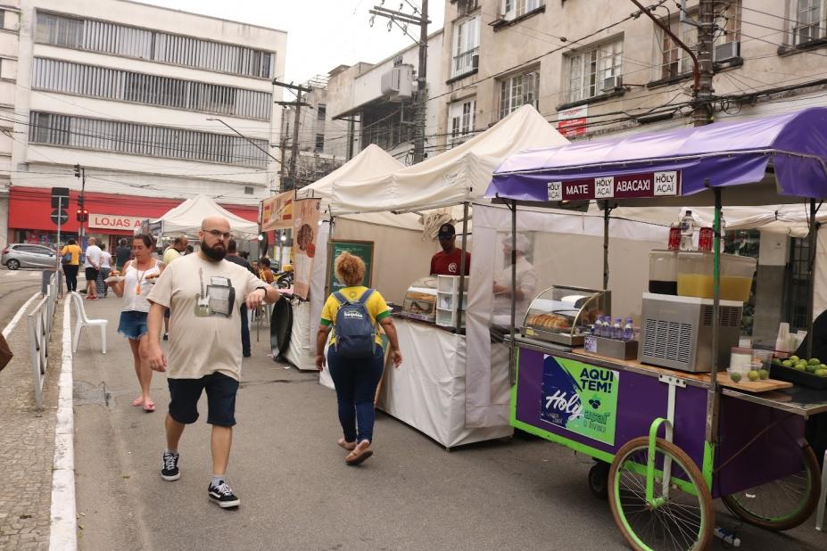 barracas de lanches montadas em praça. Pessoas circulam em torno. #paratodosverem