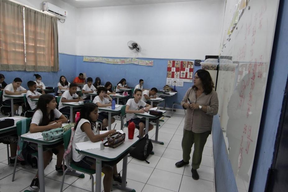 sala de aula com alunos sentadas e professora à frente da lousa. #paratodosverem 