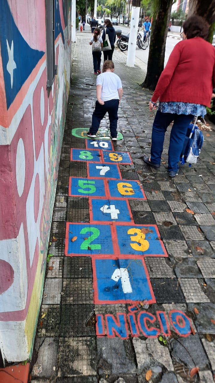 criança pulando amarelinha na calçada #paratodosverem