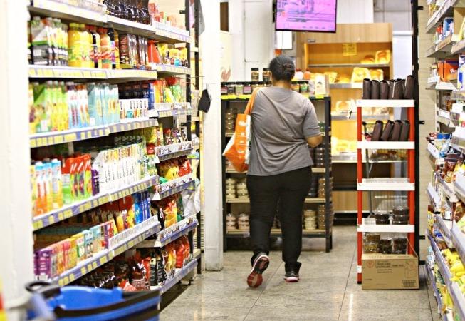 Mulher com sacola no corredor de um supermercado. #paratodosverem