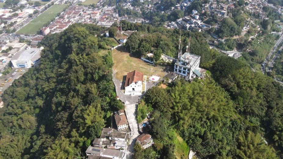 vista aérea do monte serrat, com a capela ao centro e o antigo cassino ao fundo. Área é rodeada de verde. #paratodosverem