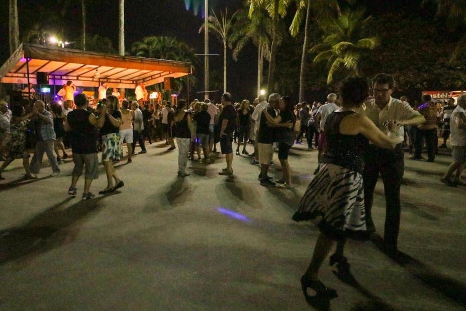Casais dançam em praça diante de palco iluminado. #paratodosverem 