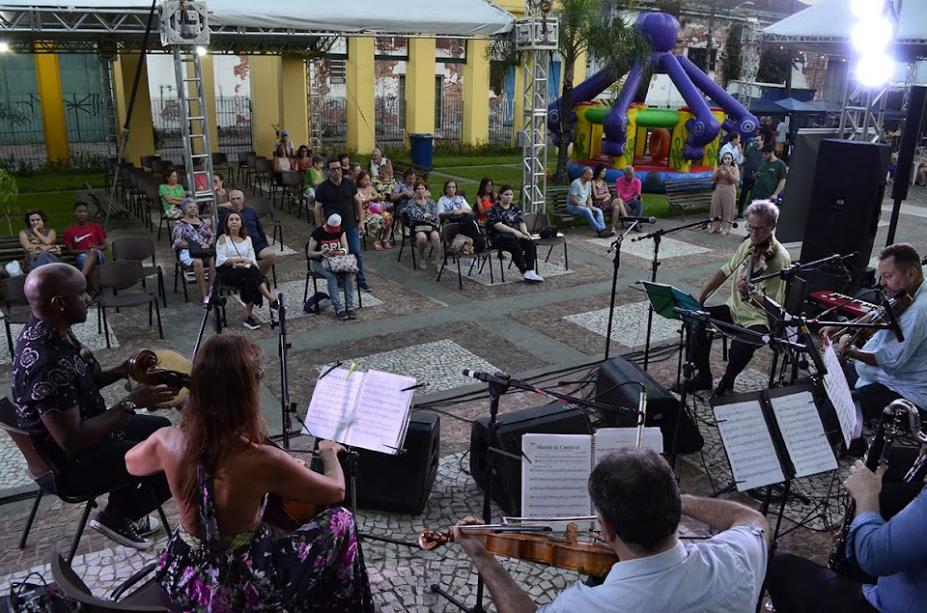 apresentação de conjunto de cordas e público ao fundo em um espaço aberto. #paratodosverem 