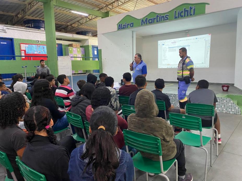 dois homens uniformizados da cet falam a jovens que estão sentados em pátio escolar. #paratodosverem 