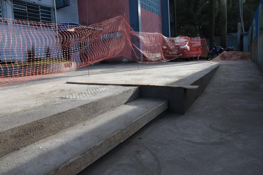 degraus e rampa em concreto em primeiro plano. No nível acima área tem uma cerca de plástico. #paratodosverem