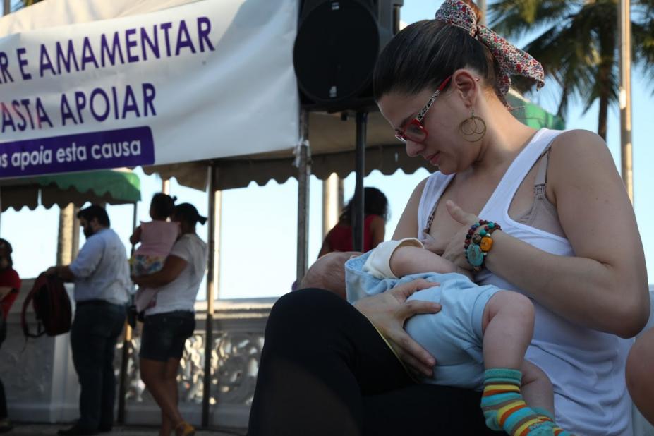 Mulher está sentada amamentando criança a céu aberto. #Paratodosverem