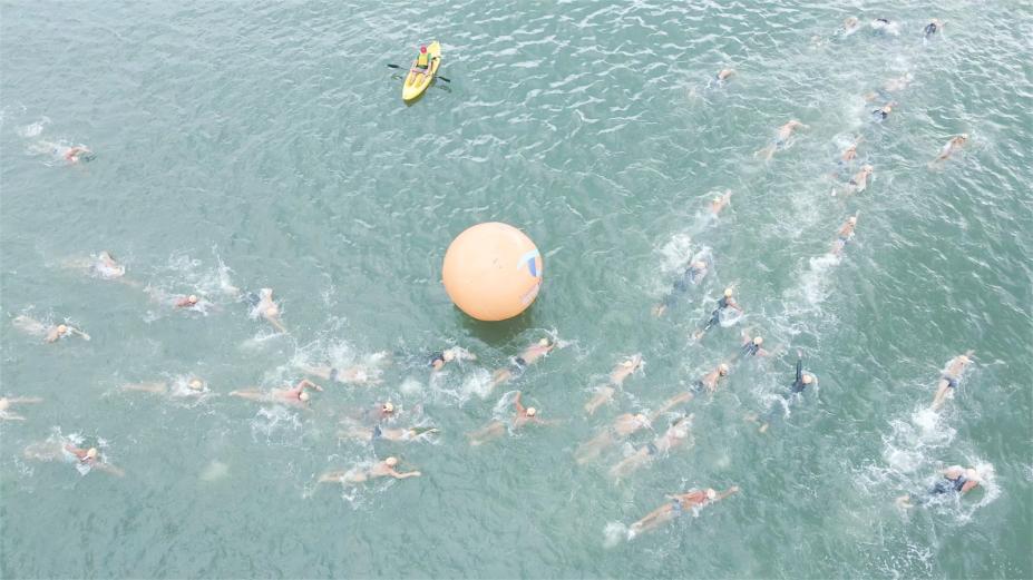 nadadores no mar. Uma grande boia marca trecho da competição. #paratodosverem