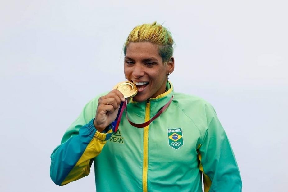 Ana Marcela 'morde' medalha de ouro vestida com uniforme da delegação do Brasil. #pracegover