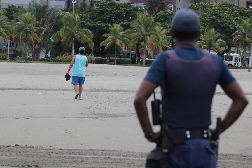 homem andando na orla, observado por guarda 