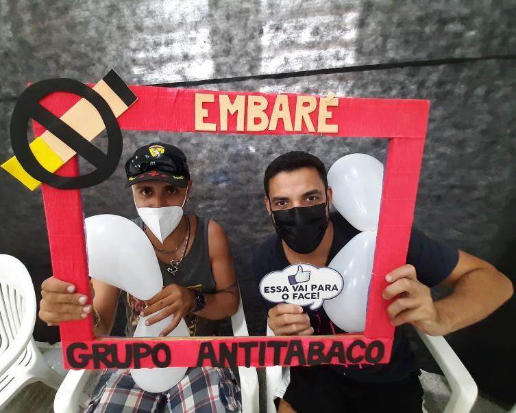 dois rapazes seguram uma moldura onde se lê no alto Embaré. Ao lado, a arte de um cigarro com um carimbo para não fumar. Na parte de baixo se lê grupo antitabaco. #paratodosverem