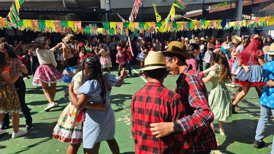crianças com roupas típicas juninas dançam em pares numa quadra. #paratodosverem 
