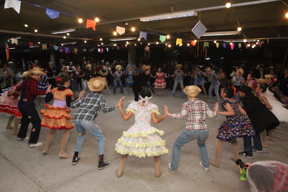 grupo com roupas típicas juninas dança quadrilha. #paratodosverem